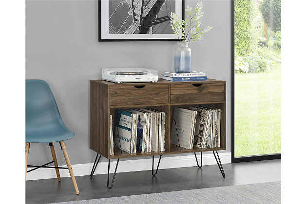 Add a blast from the past with the Novogratz Concord Turntable Stand with Drawers. Inspired from mid-century design, the laminated particleboard and MDF complement the black metal hairpin legs for a fun retro look. The medium brown woodgrain finish pairs well with any décor from modern to classic. The double wide stand offers plenty of space to place a record player, speakers, and stereo or even decorations. Keep your remotes, cassette tapes, and record mats or weights for your singles stored away and organized in the 2 drawers. The drawer cutout gives the stand a clean, no-handle look that is easy to open. Keep all of your albums organized in the large open cubbies that feature metal record dividers to keep all of your albums upright. The Novogratz Concord Turntable Stand with Drawers ships flat to your door and 2 adults are recommended for assembly upon opening. The Stand can hold up to 60 lbs. while the cubbies will hold 20 lbs. each. Each drawer can hold up to 15 lbs. Upon assembly, the Stand measures to be 31.8"H x 39.7"W x 18"D.Take it back in time with the novogratz concord turntable stand with drawers | The medium brown woodgrain laminated particleboard and mdf offer a strong build that complements the mid-century inspired black metal hairpin legs | The double wide stand offers plenty of space for a record player, speakers and stereo and features 2 large open cubbies with metal dividers to keep your albums upright and organized. Keep your remotes, cassette tapes, and record mats or weights stored away in the 2 spacious drawers | Complete your collection with other novogratz items (sold separately) | The novogratz concord turntable stand with drawers ships flat to your door and 2 adults are recommended for assembly. The stand can hold up to 60 lbs. While the cubbies will hold 20 lbs. Each. Each drawer can hold up to 15 lbs. Assembled dimensions: 31.8"h x 39.7"w x 18"d | 1 year limited warranty included
