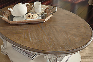 Elevating the art of traditional cottage styling, the Realyn oval coffee table is sure to serve you beautifully for years to come. Antiqued two-tone aesthetic blends a chipped white with a distressed wood finished top for added charm. Classic cabriole legs and shapely lower shelf are a lovely twist. Decorative corbels add refinement.Made of veneers, wood and engineered wood, with cast resin components | Antiqued two-tone finish | Fixed lower shelf | Assembly required | Estimated Assembly Time: 30 Minutes