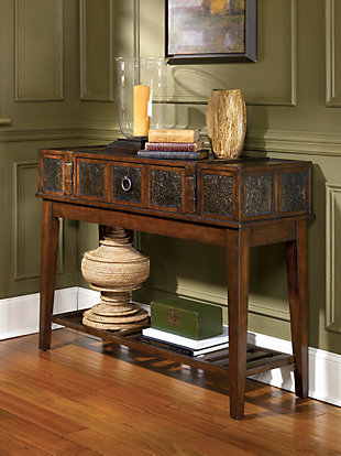 Satisfy your taste for something delightfully different with the campaign-style McKenna sofa table. Details including inset stamped metal and buckled belt accents provide such a well-traveled touch, while the decadent hue is rich with contrast and character.Made of veneers, wood, engineered wood and metal | Hand-finished | Antiqued bronze-tone hardware | Faux leather belt accents | 1 drawer | 1 fixed shelf | Assembly required