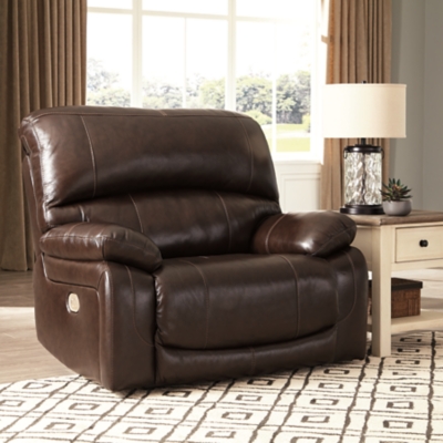 Fashion-forward style. Sumptuous leather feel and appeal. Total comfort at your fingertips. It’s all yours for the taking with the Hallstrung power recliner with adjustable headrest. Wrapped in a lavish chocolate-colored upholstery, this decidedly contemporary power recliner tantalizes the senses in so many ways. Rest assured, the wide seating area is covered in 100% leather for your pleasure, while a skillfully matched faux leather on the exterior makes luxury affordable. Upping the comfort with 44" high back styling, this power recliner truly caters from head to toe. An Easy View™ power adjustable headrest allows you to lean back while propping up your head—perfect for chilling out in front of the TV—while an extended ottoman lets you stretch out all the more. And with a USB port in the power control panel, you hardly have to move a muscle to stay powered up.High-resiliency foam cushions wrapped in thick poly fiber | Corner-blocked frame with metal reinforced seat | One-touch power control with adjustable positions | 44" high back design | Attached back and seat cushions | Easy View™ power adjustable headrest | Extended ottoman for enhanced comfort | Leather interior upholstery; polyester/vinyl exterior upholstery | Includes USB charging port in each power control | Power cord included; UL Listed | Estimated Assembly Time: 15 Minutes