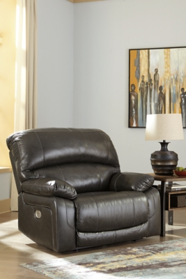 Fashion-forward style. Sumptuous leather feel and appeal. Total comfort at your fingertips. It’s all yours for the taking with the Hallstrung power recliner with adjustable headrest. Wrapped in an attractive gray upholstery, this decidedly contemporary power recliner tantalizes the senses in so many ways. Rest assured, the wide seating area is covered in 100% leather for your pleasure, while a skillfully matched faux leather on the exterior makes luxury affordable. Upping the comfort with 44" high back styling, this power recliner truly caters from head to toe. An Easy View™ power adjustable headrest allows you to lean back while propping up your head—perfect for chilling out in front of the TV—while an extended ottoman lets you stretch out all the more. And with a USB port in the power control panel, you hardly have to move a muscle to stay powered up.High-resiliency foam cushions wrapped in thick poly fiber | Corner-blocked frame with metal reinforced seat | One-touch power control with adjustable positions | 44" high back design | Attached back and seat cushions | Easy View™ power adjustable headrest | Leather interior upholstery; polyester/vinyl exterior upholstery | Extended ottoman for enhanced comfort | Includes USB charging port in the power control | Power cord included; UL Listed | Estimated Assembly Time: 15 Minutes