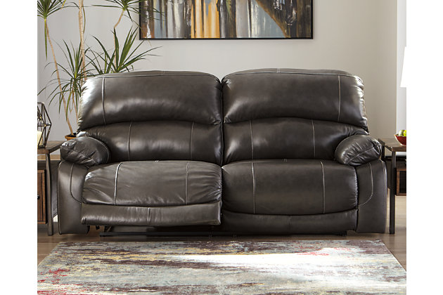Fashion-forward style. Sumptuous leather feel and appeal. Total comfort at your fingertips. It’s all yours for the taking with the Hallstrung power reclining sofa. Wrapped in a rich charcoal gray upholstery, this decidedly contemporary power sofa tantalizes the senses in so many ways. Rest assured, the seating area is covered in 100% leather for your pleasure, while a skillfully matched faux leather on the exterior makes luxury affordable. Upping the comfort with 44" high back styling, this power sofa truly caters from head to toe. An Easy View™ power adjustable headrest allows you to lean back while propping up your head—perfect for chilling out in front of the TV—while an extended ottoman lets you stretch out all the more. And with a USB port in each power control panel, you hardly have to move a muscle to stay powered up.Dual-sided recliner | One-touch power control recliners with adjustable positions | Includes USB charging port in each power control | Corner-blocked frames with metal reinforced seats | Attached backs and seat cushions | High-resiliency foam cushions wrapped in thick poly fiber | Easy View™ power adjustable headrests | Extended ottomans for enhanced comfort | 100% genuine top-grain leather throughout the seating areas and armrests | High quality leather substitute covers remaining areas | Power cord included; UL Listed | Estimated Assembly Time: 15 Minutes