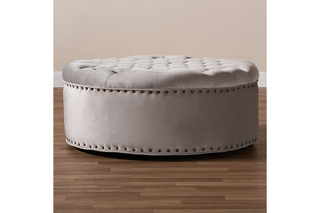 A cut above the rest, this round cocktail ottoman will exceed your expectations. This beautiful living area centerpiece is made with a sturdy wood frame, firm foam cushioning and velvet fabric upholstery. Finishing touches include nailhead trim and wood, non-marking feet.Eucalyptus wood frame | Light gray velvet upholstery | Antiqued brass-tone nailhead trim | Black finished feet | No assembly required