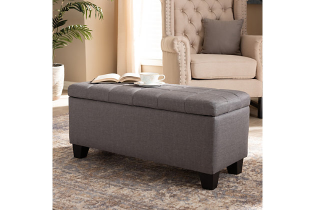This modern ottoman displays a simple, streamlined design that makes it complementary to a wide range of decor styles. Upholstered in a soft, neutral fabric, the lid is foam padded and biscuit tufted to provide the utmost comfort. The ottoman features a large compartment under the lid, providing space to store extra blankets and pillows. Finished wood feet complete the look. Versatile enough to use as both seating and storage in the entryway, living room or bedroom.Gray polyester upholstery | Lift-top storage compartment | Wood feet with black finish | Assembly required