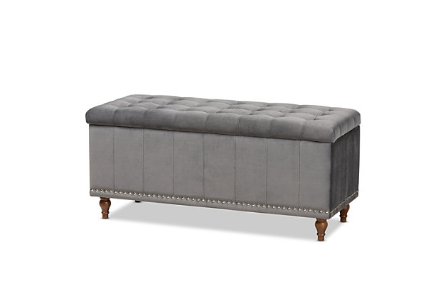 Whether it's placed in the bedroom or living room, the versatile Kaylee bench offers elegant style and handy storage space. Constructed with rubberwood, this storage bench is upholstered in a soft gray velvet fabric that adds a dose of glamour to your space. The top is padded with foam for seating comfort, and opens to reveal ample storage space for extra blankets and linens. Silvertone nailhead trim and grid stitching lend a modern look, while button tufting and turned feet add a refined elegance.Contemporary style | Walnut brown legs | Made of rubberwood, engineered wood, polyester and foam | Upholstered in gray velvet polyester fabric; foam padding | Lift-top storage compartment | Imported | Requires leg assembly