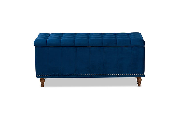 Whether it's placed in the bedroom or living room, the versatile Kaylee bench offers elegant style and handy storage space. Constructed with rubberwood, this storage bench is upholstered in a soft blue velvet fabric that adds a dose of glamour to your space. The top is padded with foam for seating comfort, and opens to reveal ample storage space for extra blankets and linens. Silvertone nailhead trim and grid stitching lend a modern look, while button tufting and turned feet add a refined elegance.Contemporary style | Walnut brown legs | Made of rubberwood, engineered wood, polyester and foam | Upholstered in blue velvet polyester fabric; foam padding | Lift-top storage compartment | Imported | Requires leg assembly