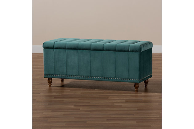 Whether it's placed in the bedroom or living room, the versatile Kaylee bench offers elegant style and handy storage space. Constructed with rubberwood, this storage bench is upholstered in a soft teal velvet fabric that adds a dose of glamour to your space. The top is padded with foam for seating comfort, and opens to reveal ample storage space for extra blankets and linens. Silver nailhead trim and grid stitching lend a modern look, while button tufting and turned feet add a refined elegance.Contemporary style | Walnut brown legs | Made of rubberwood, engineered wood, polyester and foam | Upholstered in teal velvet polyester fabric; foam padding | Lift-top storage compartment | Imported | Requires leg assembly