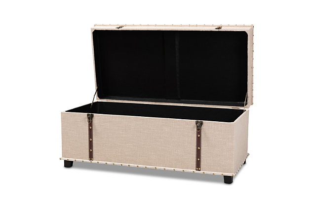 An ottoman, coffee table and storage trunk all in one, the Kyra storage ottoman adds versatility to any space. Set on top of black tapered feet, this ottoman is upholstered in an elegant linen-like fabric and features a cushioned lift-top seat that reveals ample storage space. Inspired by vintage steamer trunks, the Kyra is accented with faux leather straps and brass-tone latches. Goldtone nailheads and button tufting add an extra dose of style.Made of engineered wood and metal | Upholstered in velvet polyester fabric; foam padding | Goldtone nailhead trim; button tufting | Imported | Arrives fully assembled