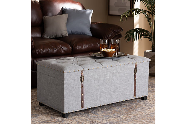 An ottoman, coffee table and storage trunk all in one, the Kyra storage ottoman adds versatility to any space. Set on top of black tapered feet, this ottoman is upholstered in an elegant linen-like fabric and features a cushioned lift-top seat that reveals ample storage space. Inspired by vintage steamer trunks, this ottoman is accented with faux leather straps and brass-tone latches. Goldtone nailheads and button tufting add an extra dose of style.Made of engineered wood and metal | Upholstered in velvet polyester fabric; foam padding | Goldtone nailhead trim; button tufting | Imported | Arrives fully assembled