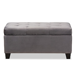 Cute, sturdy, and practical, the Michaela storage ottoman can meet a wide range of your organization needs. The modern and contemporary-inspired design emphasizes a simple silhouette and luxurious texture. The ottoman is upholstered in a rich velvet fabric, with a foam-padded, button-tufted lid. Ample storage space is located beneath the lid, made secure with a spring hinge. Black finished polymer feet complete the look. Use this ottoman as a decorative piece at the edge of a bed, as storage in the guest room, or as storage for shoes and toys in your entryway. The Michaela storage ottoman is made in China and requires assembly.Contemporary style | Made of oak wood and polymer | Upholstered in gray velvet polyester fabric; foam padding | Lift-up storage compartment | Black wooden feet | Imported | Assembly required