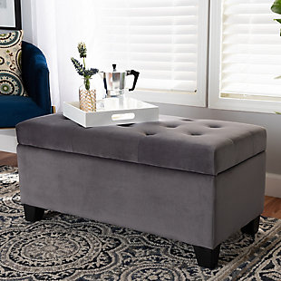 Cute, sturdy, and practical, the Michaela storage ottoman can meet a wide range of your organization needs. The modern and contemporary-inspired design emphasizes a simple silhouette and luxurious texture. The ottoman is upholstered in a rich velvet fabric, with a foam-padded, button-tufted lid. Ample storage space is located beneath the lid, made secure with a spring hinge. Black finished polymer feet complete the look. Use this ottoman as a decorative piece at the edge of a bed, as storage in the guest room, or as storage for shoes and toys in your entryway. The Michaela storage ottoman is made in China and requires assembly.Contemporary style | Made of oak wood and polymer | Upholstered in gray velvet polyester fabric; foam padding | Lift-up storage compartment | Black wooden feet | Imported | Assembly required