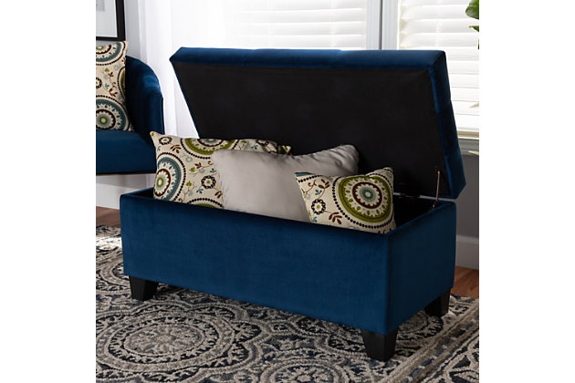 Cute, sturdy, and practical, the Michaela storage ottoman can meet a wide range of your organization needs. The modern and contemporary-inspired design emphasizes a simple silhouette and luxurious texture. The ottoman is upholstered in a rich velvet fabric, with a foam-padded, button-tufted lid. Ample storage space is located beneath the lid, made secure with a spring hinge. Black finished polymer feet complete the look. Use this ottoman as a decorative piece at the edge of a bed, as storage in the guest room, or as storage for shoes and toys in your entryway. The Michaela storage ottoman is made in China and requires assembly.Contemporary style | Made of oak wood and polymer | Upholstered in blue velvet polyester fabric; foam padding | Lift-up storage compartment | Black wooden feet | Imported | Assembly required