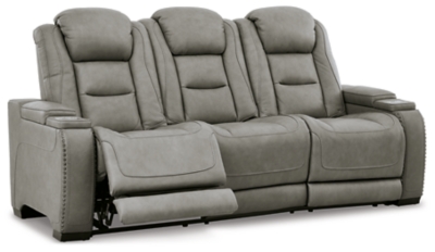 Reserved for him and made for her, The Man-Den power reclining sofa in gray delivers all the comfort and style you could ask for. Inspired by sports car interiors, the seating area is covered in real leather for your pleasure, with a “perforated automotive” treatment for that much more appeal. Positioned at your fingertips, the advanced one-touch power control puts you in the driver’s seat with everything from an Easy View™ power headrest and power lumbar support, to a USB port and wireless charging for your phone. Talk about fully loaded. The middle seat reveals a pull-down table with dimmable reading lights and cup holders. And with integrated cup holders and hidden storage compartments under the posh, padded armrests, this designer power reclining sofa makes the most of every inch of space.Dual-sided recliner | One-touch power control with Easy View™ power adjustable headrest, power lumbar support, USB charging and wireless phone charging | Wireless charger accommodates later model smartphones, including Apple iPhone, Samsung Galaxy, Huawei Mate and Nokia Lumia | Corner-blocked frame with metal reinforced seat | Attached cushions | 43" high back | High-resiliency foam cushions wrapped in thick poly fiber | Leather interior upholstery (with perforated details); vinyl/polyester exterior upholstery | Pull-down table with 2 cup holders (with 2 layers to accommodate drink containers) dimmable reading lights and magazine storage | Each armrest includes storage compartment | Extended ottoman for enhanced comfort | Nailhead trim | Power cord included; UL Listed | Estimated Assembly Time: 15 Minutes