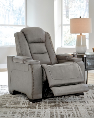 Reserved for him and made for her, The Man-Den power recliner in gray delivers all the comfort and style you could ask for. Inspired by sports car interiors, the seating area is covered in real leather for your pleasure, with a “perforated automotive” treatment for that much more appeal. Positioned at your fingertips, the advanced one-touch power control puts you in the driver’s seat with everything from an Easy View™ power headrest and power lumbar support, to a USB port and wireless charging for your phone. And with an integrated cup holder and hidden storage compartments under the posh, padded armrests, this designer power recliner makes the most of every inch of space.One-touch power control with Easy View™ power adjustable headrest, power lumbar support, USB charging and wireless phone charging | Wireless charger accommodates later model smartphones, including Apple iPhone, Samsung Galaxy, Huawei Mate and Nokia Lumia | Corner-blocked frame with metal reinforced seat | Attached cushions | 43" high back | High-resiliency foam cushions wrapped in thick poly fiber | Leather interior upholstery (with perforated details); vinyl/polyester exterior upholstery | Each armrest includes storage compartment | Cup holder (with 2 layers to accommodate drink containers) | Extended ottoman for enhanced comfort | Nailhead trim | Power cord included; UL Listed | Estimated Assembly Time: 15 Minutes