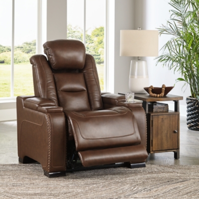 Reserved for him and made for her, this mahogany hued power recliner delivers all the comfort and style you could ask for. Inspired by sports car interiors, the Man-Den power recliner features real leather in the seating area for your pleasure. The advanced one-touch power control puts you in the driver’s seat with an adjustable headrest and lumbar support, USB port and wireless charging for your phone, plus an integrated cup holder, all at your fingertips. This power recliner utilizes every inch of space, with hidden storage compartments under the padded armrests.One-touch power control with Easy View™ power adjustable headrest, power lumbar support, USB charging and wireless phone charging | Wireless charger accommodates later model smartphones, including Apple iPhone, Samsung Galaxy, Huawei Mate and Nokia Lumia | Corner-blocked frame with metal reinforced seat | Attached cushions | High-resiliency foam cushions wrapped in thick poly fiber | Leather interior upholstery (with perforated details); vinyl/polyester (faux leather) exterior upholstery | Armrest with storage compartment | 2 cup holders | 43" high back | Extended ottoman for enhanced comfort | Nailhead trim | Power cord included; UL Listed | Estimated Assembly Time: 15 Minutes