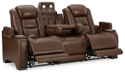 Reserved for him and made for her, this mahogany hued power reclining sofa delivers all the comfort and style you could ask for. Inspired by sports car interiors, the Man-Den power reclining sofa features real leather in the seating area for your pleasure with high-end accents for that much more appeal. The advanced one-touch power control puts you in the driver’s seat with an adjustable headrest and lumbar support, USB port and wireless charging for your phone, all at your fingertips. The pull-down table in the middle seat includes dimmable reading lights and integrated cup holders. This power recliner makes the most of every inch of space, with hidden storage compartments under the padded armrests.Dual-sided recliner | One-touch power control with Easy View™ power adjustable headrest, power lumbar support, USB charging and wireless phone charging | Wireless charger accommodates later model smartphones, including Apple iPhone, Samsung Galaxy, Huawei Mate and Nokia Lumia | Corner-blocked frame with metal reinforced seat | Attached cushions | High-resiliency foam cushions wrapped in thick poly fiber | Leather interior upholstery (with perforated details); vinyl/polyester exterior upholstery | Pull-down table with 2 cup holders, dimmable reading lights and magazine storage | 43" high back | Armrest with storage compartment | Extended ottoman for enhanced comfort | Nailhead trim | Power cord included; UL Listed | Estimated Assembly Time: 15 Minutes