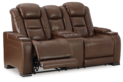 Reserved for him and made for her, this mahogany hued power reclining loveseat delivers all the comfort and style you could ask for. Inspired by sports car interiors, the Man-Den power reclining loveseat with console features real leather in the seating area for your pleasure with high-end accents for that much more appeal. The advanced one-touch power control puts you in the driver’s seat with an adjustable headrest and lumbar support, USB port and wireless charging for your phone, all at your fingertips. The center console includes two illuminated cup holders and a storage compartment. This power recliner makes the most of every inch of space, with hidden storage compartments under the padded armrests.Dual-sided recliner | One-touch power control with Easy View™ power adjustable headrest, power lumbar support, USB charging and wireless phone charging | Wireless charger accommodates later model smartphones, including Apple iPhone, Samsung Galaxy, Huawei Mate and Nokia Lumia | Corner-blocked frame with metal reinforced seat | Attached cushions | High-resiliency foam cushions wrapped in thick poly fiber | Leather interior upholstery (with perforated details); vinyl/polyester exterior upholstery | Storage console with 2 cup holders | 43" high back | Armrest with storage compartment | Extended ottoman for enhanced comfort | Nailhead trim | Power cord included; UL Listed | Estimated Assembly Time: 15 Minutes