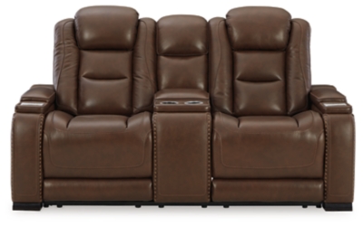 Reserved for him and made for her, this mahogany hued power reclining loveseat delivers all the comfort and style you could ask for. Inspired by sports car interiors, the Man-Den power reclining loveseat with console features real leather in the seating area for your pleasure with high-end accents for that much more appeal. The advanced one-touch power control puts you in the driver’s seat with an adjustable headrest and lumbar support, USB port and wireless charging for your phone, all at your fingertips. The center console includes two illuminated cup holders and a storage compartment. This power recliner makes the most of every inch of space, with hidden storage compartments under the padded armrests.Dual-sided recliner | One-touch power control with Easy View™ power adjustable headrest, power lumbar support, USB charging and wireless phone charging | Wireless charger accommodates later model smartphones, including Apple iPhone, Samsung Galaxy, Huawei Mate and Nokia Lumia | Corner-blocked frame with metal reinforced seat | Attached cushions | High-resiliency foam cushions wrapped in thick poly fiber | Leather interior upholstery (with perforated details); vinyl/polyester exterior upholstery | Storage console with 2 cup holders | 43" high back | Armrest with storage compartment | Extended ottoman for enhanced comfort | Nailhead trim | Power cord included; UL Listed | Estimated Assembly Time: 15 Minutes