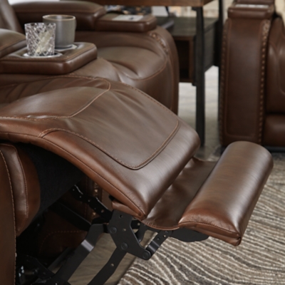 Reserved for him and made for her, this mahogany hued power reclining sofa delivers all the comfort and style you could ask for. Inspired by sports car interiors, the Man-Den power reclining sofa features real leather in the seating area for your pleasure with high-end accents for that much more appeal. The advanced one-touch power control puts you in the driver’s seat with an adjustable headrest and lumbar support, USB port and wireless charging for your phone, all at your fingertips. The pull-down table in the middle seat includes dimmable reading lights and integrated cup holders. This power recliner makes the most of every inch of space, with hidden storage compartments under the padded armrests.Dual-sided recliner | One-touch power control with Easy View™ power adjustable headrest, power lumbar support, USB charging and wireless phone charging | Wireless charger accommodates later model smartphones, including Apple iPhone, Samsung Galaxy, Huawei Mate and Nokia Lumia | Corner-blocked frame with metal reinforced seat | Attached cushions | High-resiliency foam cushions wrapped in thick poly fiber | Leather interior upholstery (with perforated details); vinyl/polyester exterior upholstery | Pull-down table with 2 cup holders, dimmable reading lights and magazine storage | 43" high back | Armrest with storage compartment | Extended ottoman for enhanced comfort | Nailhead trim | Power cord included; UL Listed | Estimated Assembly Time: 15 Minutes